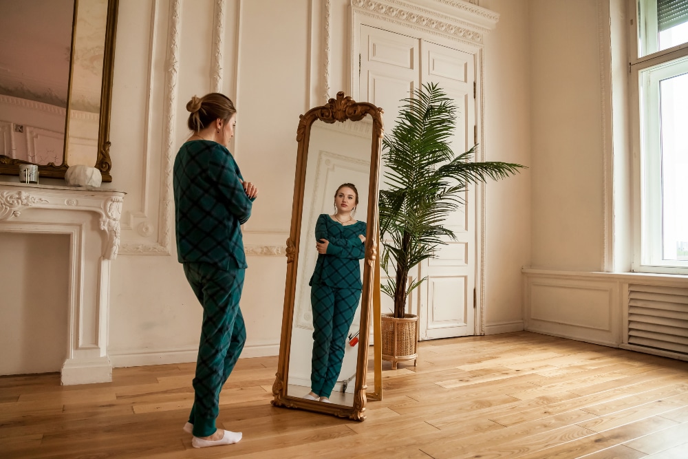 Lonely woman looking at mirror in her reflection in living room at home.