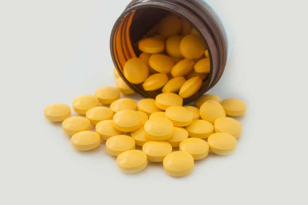 Yellow pills spilling out of a toppled from pill bottle